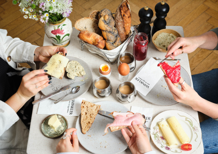 Bäckerei Winkler Frühstückstisch mit Gebäck und Händen die Besteck halten.